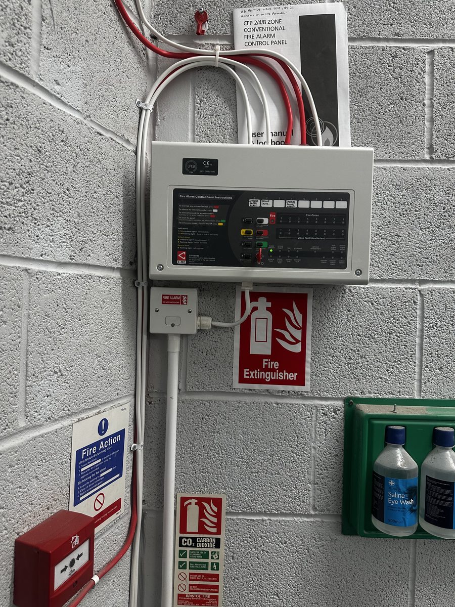 Conventional zone fire alarm control panel installed with manual call point, fire extinguisher signage and eye wash station — BS 5839 commercial fire alarm system by DS Electrical Somerset