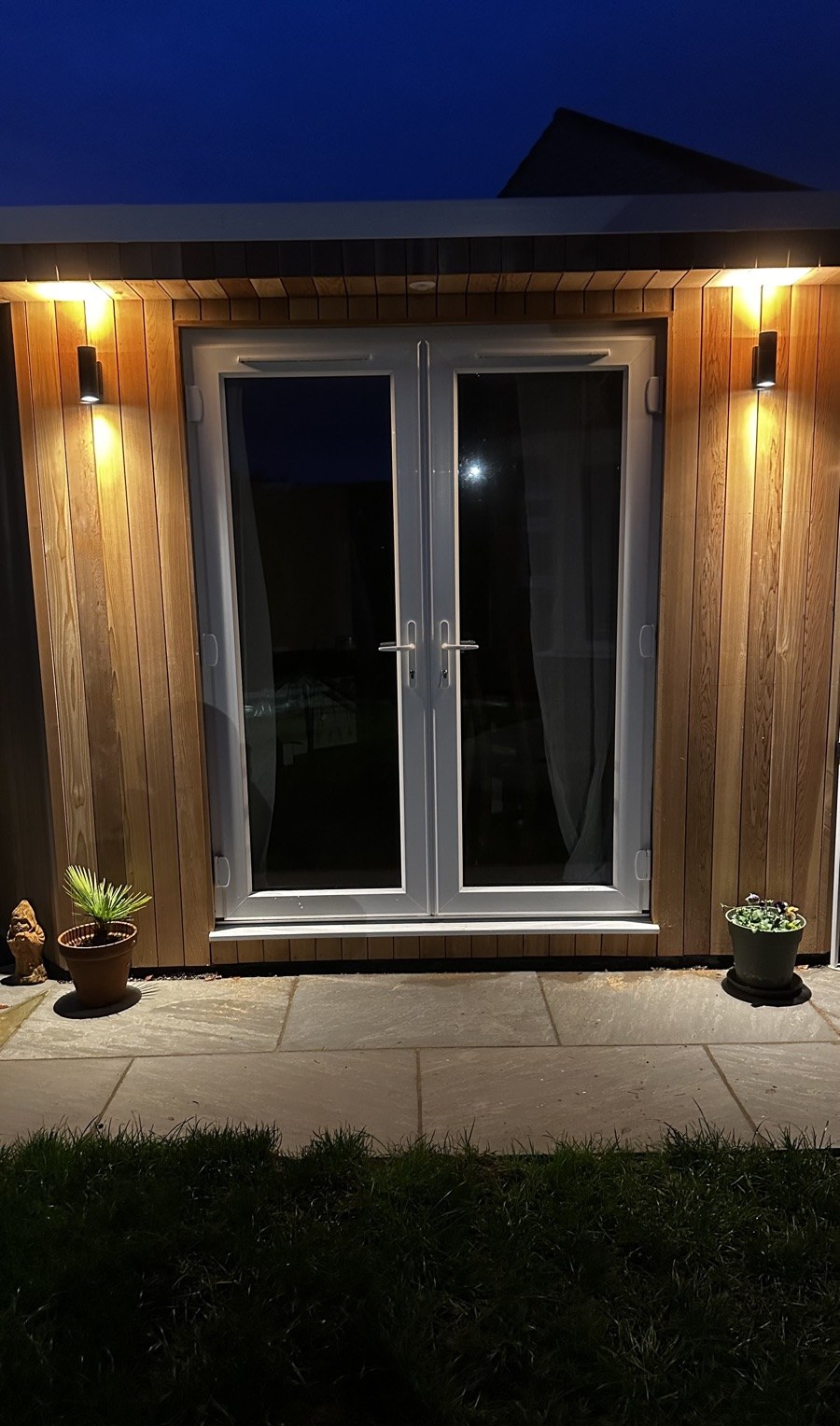 Garden room with warm wall lights on cedar cladding at dusk